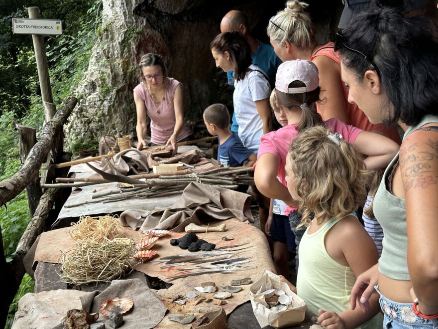 Children and adults at a table outside the cave. On the table are many prehistoric items and tools to look at and touch