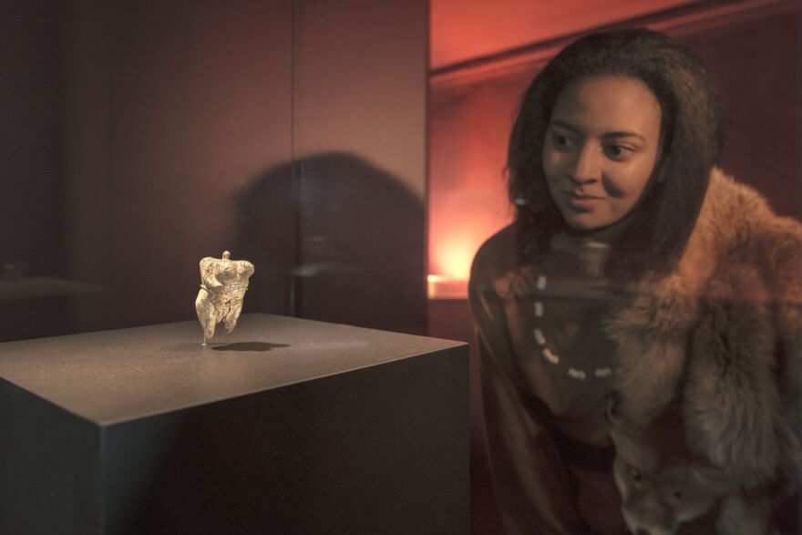 A woman in prehistory attire looking at the venus figure in a museum display case