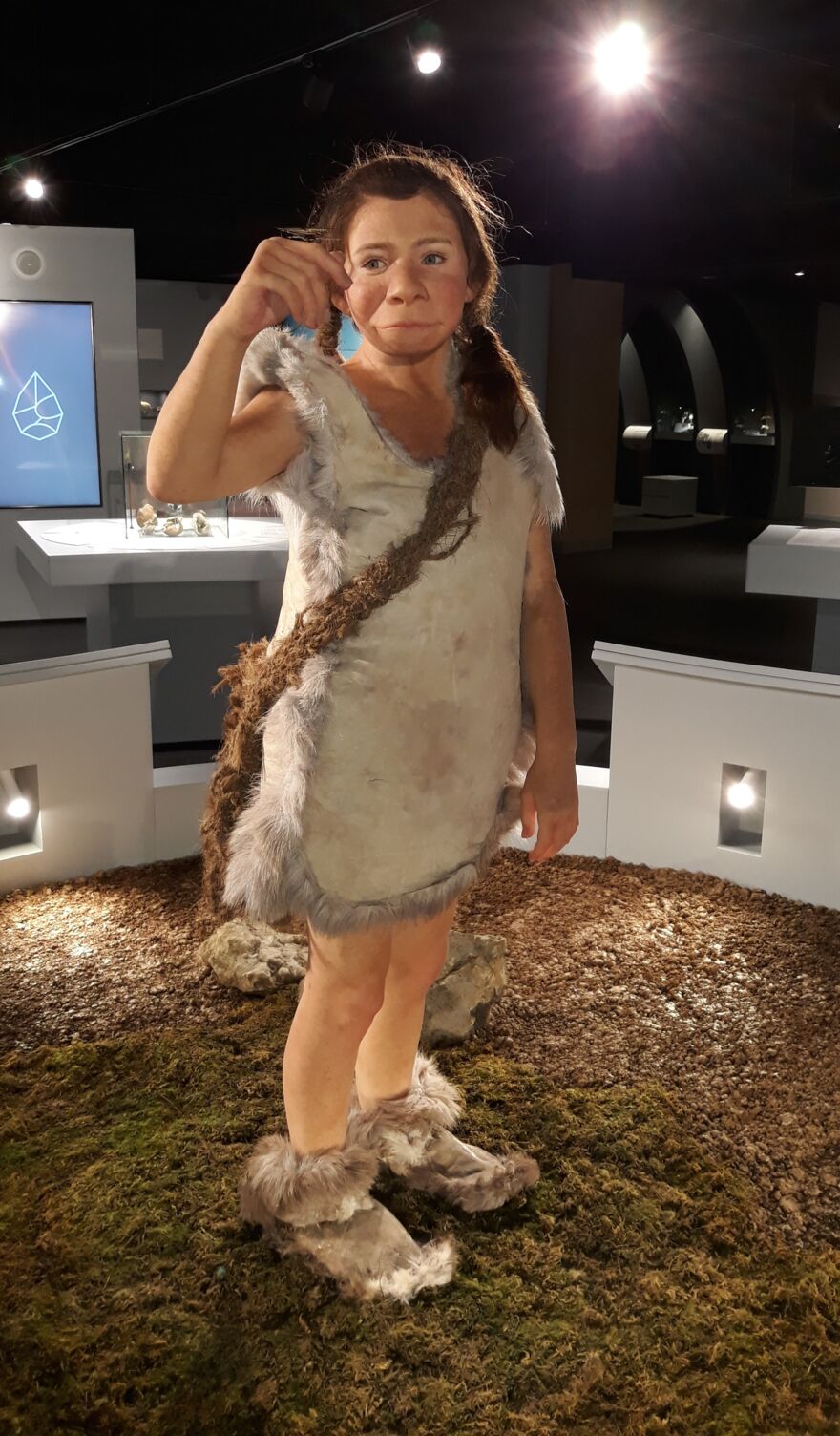 Life-size figurine of a Neanderthal child, looking at a butterfly on its hand.