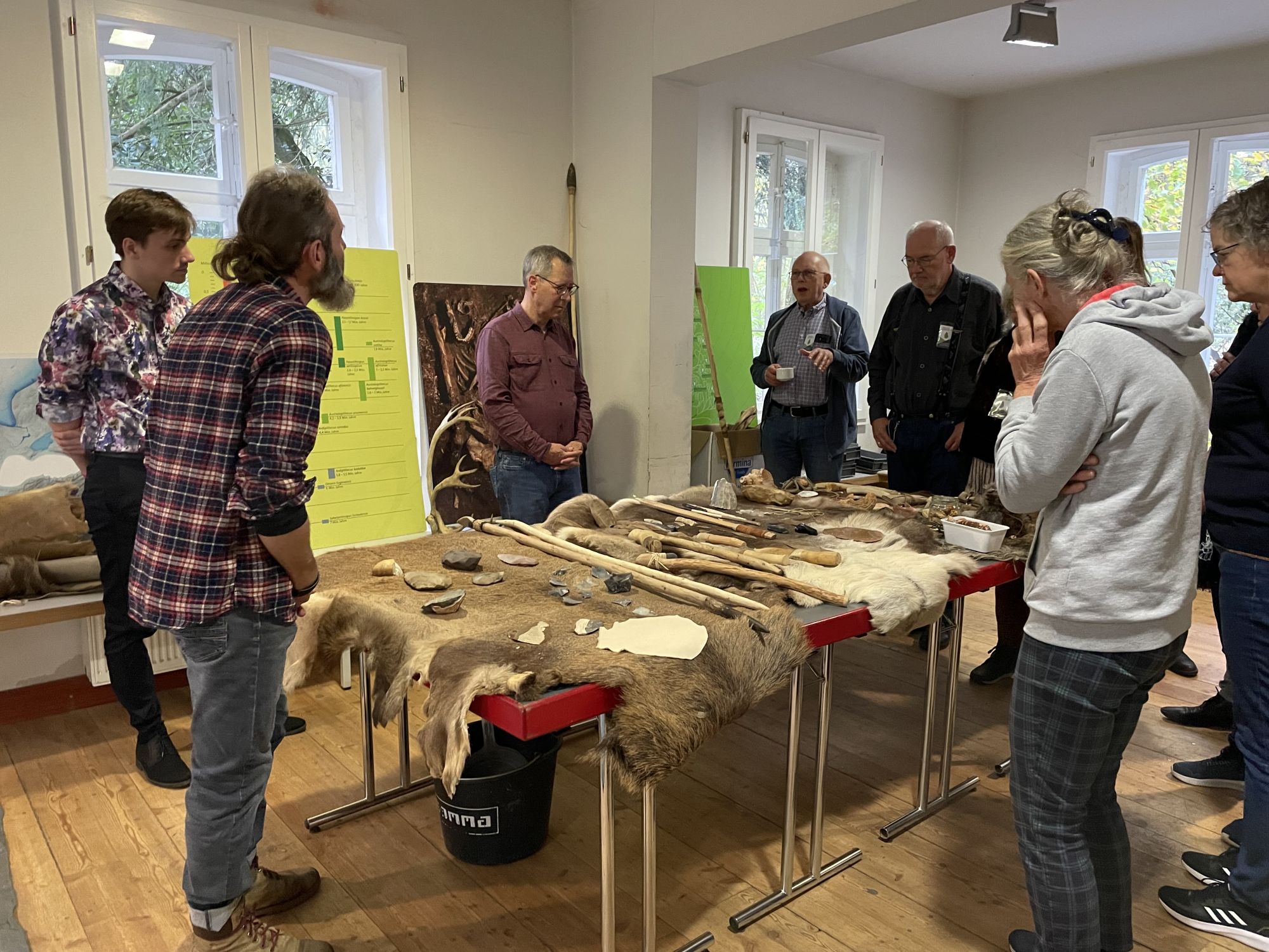 Participants standing around a table. On the table is a variety of prehistoric tools and fabrics