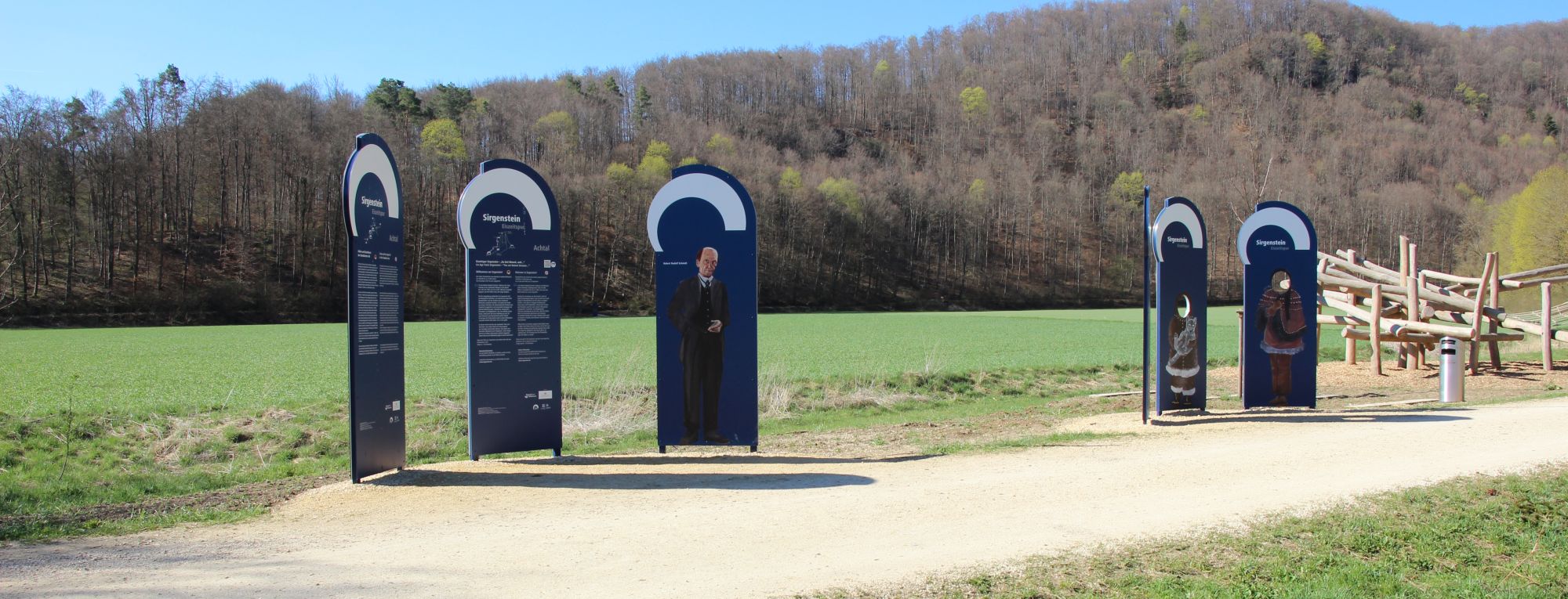 A row of outdoor information panels, a playground in the back