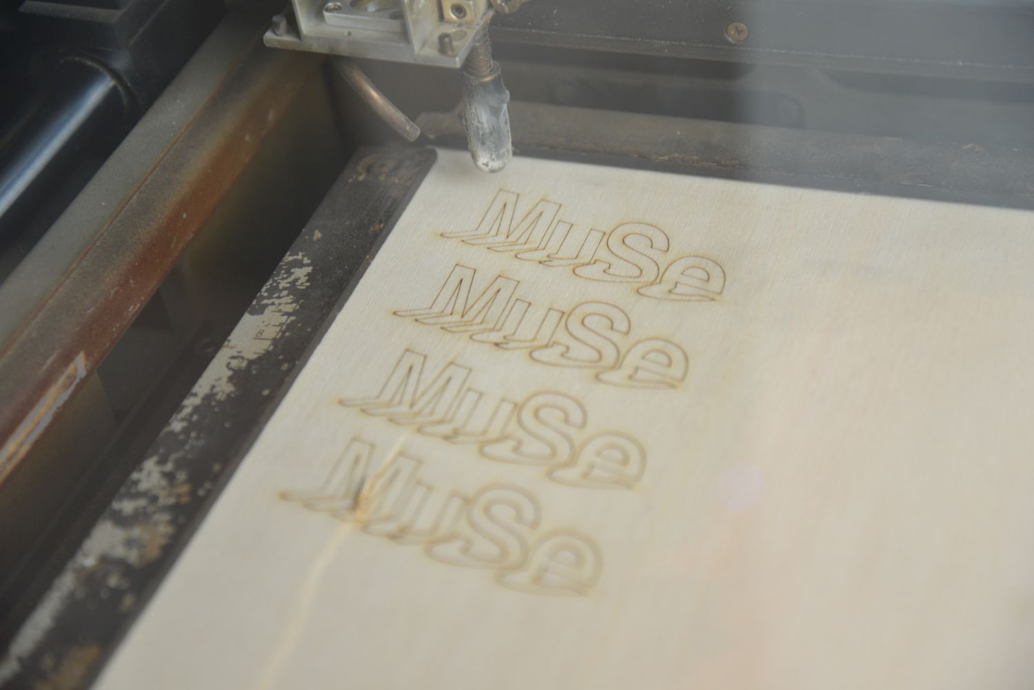 A laser cutter repeatedly engraves the museum's logo onto a piece of wooden board.
